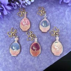 four glass bottle shaped charms sitting on top of a purple cloth next to some flowers