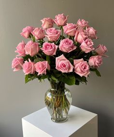 a vase filled with pink roses sitting on top of a white table next to a gray wall