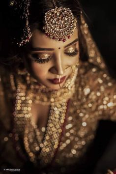 a woman in gold and red makeup looks down at her hand while wearing a head piece