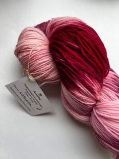 two skeins of red and pink yarn on a white surface with a tag