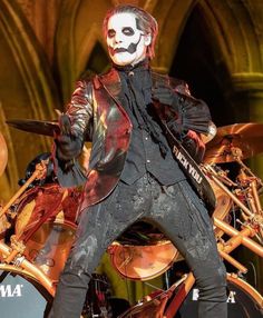 a man dressed in black and white with makeup on his face standing next to a drum set