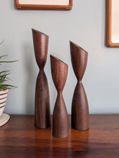 three wooden sculptures on a table next to a potted plant and framed pictures in the background