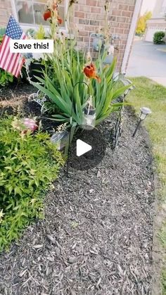 a flower bed with flowers in it and an american flag on the side of a house