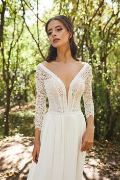 a woman in a white wedding dress standing on a path with trees and bushes behind her