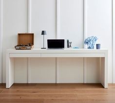 a white desk with a laptop and other items on it in front of a wall