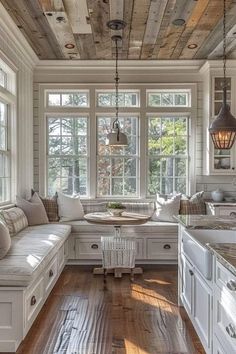 a kitchen with white cabinets and wooden floors, windows above the sink, and a breakfast nook on the far side