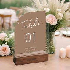 a table number sitting on top of a wooden table next to some flowers and candles