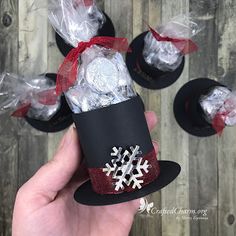 someone is holding some candy wrapped in black paper and red ribbon with white snowflakes on it