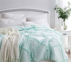 a bed with white sheets and pillows in a bedroom next to a potted plant