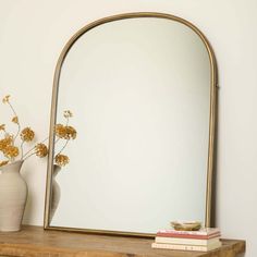 a mirror sitting on top of a wooden shelf next to a vase with flowers in it