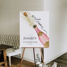 a birthday party sign on an easel in front of a couch with a bottle of champagne