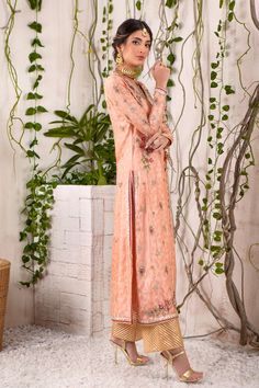 A captivating shade of peach over a canvas of jacquard silk net, this chogha features myriad of colorful resham work in beautiful floral embroidery, further enhanced with dabka, sequins, pearls, beads & crystals in rose gold, antique gold &silver tones on neckline, hem, sleeves & back. Beautifully Hand-crafted tassels for additional style element. A classy Raspberry & Gold Jacquard Chunri dupatta adds a beautiful pop of color and dhanak embellished tissue izaar elevates the festive look of this Elegant Semi-stitched Sharara With Floral Embroidery, Elegant Pink Embroidered Dola Silk Fabric, Elegant Raw Silk Salwar Kameez With Floral Embroidery, Elegant Salwar Kameez With Floral Embroidery In Raw Silk, Pink Dola Silk Kurta With Intricate Embroidery, Bollywood Style Peach Traditional Wear With Intricate Embroidery, Bollywood Traditional Wear With Intricate Embroidery In Peach, Elegant Pink Lawn Suit With Dabka Work, Peach Traditional Wear With Resham Embroidery For Reception