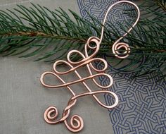 a pair of copper wire earrings sitting on top of a piece of fabric next to a pine branch