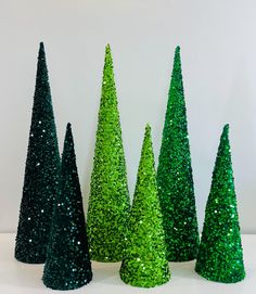 green glitter trees are lined up on a white surface with one standing out from the others