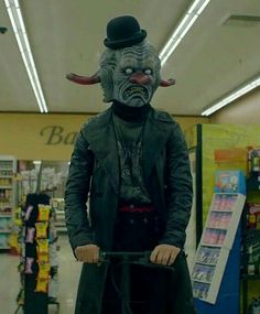 a man wearing a mask and riding a bike in a store with an evil look on his face