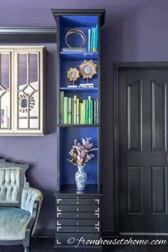 a blue bookcase with many books on it and a chair in front of it