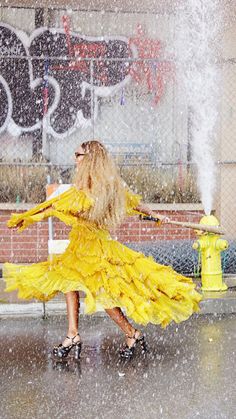 a woman in a yellow dress is dancing in the rain