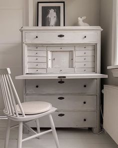 a white chair sitting in front of a desk with drawers and a dresser on top of it