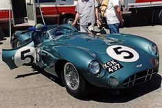 two men standing next to an old race car with numbers on the front and side