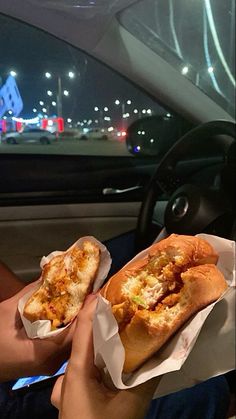 two people holding sandwiches in their hands while sitting in the backseat of a car at night