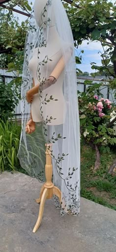 a mannequin wearing a veil and dress on a wooden stand in front of some bushes