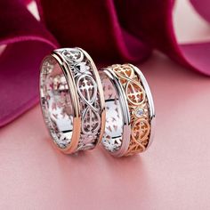 two wedding bands with intricate designs on them, sitting next to a pink velvet bag