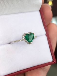 someone is holding a ring with a heart shaped green stone in it's center