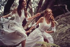 two women in white dresses are running through the woods with their hands in each other's pockets