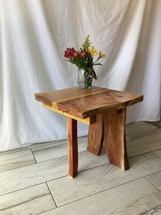 a vase with flowers sitting on top of a wooden table in front of a white backdrop