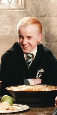 a young boy sitting at a table with food in front of him and smiling for the camera