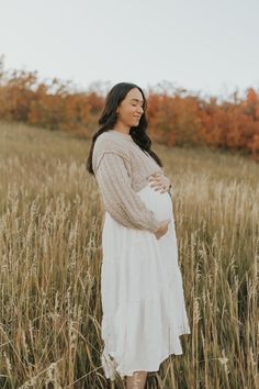 a pregnant woman standing in tall grass