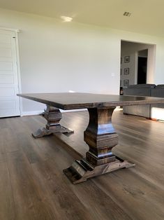 a large wooden table sitting on top of a hard wood floor covered in white walls