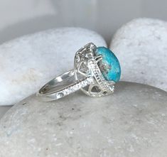 "An OOAK cabochon oval-shaped natural 6.07ct Turquoise Ring adorned with a halo of petite white topaz complimented with heart cut outs around the basket, handcrafted in sterling silver is a striking engagement/promise/statement ring. Wrapped in a box ready for gift-giving. This ring is a FINAL SALE. (r.egt.85) View our vast collection of Turquoise Rings: We can also make your custom dream ring https://www.etsy.com/shop/Belesas?ref=seller-platform-mcnav&search_query=turquoise+ring Ring Info - Elegant Oval Turquoise Ring With Large Stone, Fine Jewelry Turquoise Ring With Oval Cabochon, Elegant Round Turquoise Ring With Natural Stones, Fine Jewelry Turquoise Oval Cabochon Ring, Anniversary Oval Cabochon Turquoise Ring In Fine Jewelry Style, Oval Turquoise Ring With Bezel Setting For Anniversary, Elegant Oval Turquoise Ring With Accent Stones, Oval Turquoise Ring With Accent Stones, Anniversary Turquoise Ring With Gemstone Accents