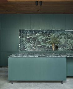 a kitchen with green cabinets and marble counter tops in the center, along with an island