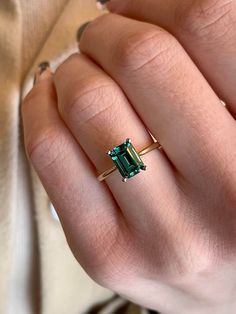 a woman's hand holding an emerald and diamond ring in her left hand,