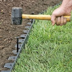 a man is holding a hammer and digging in the ground with some grass behind him