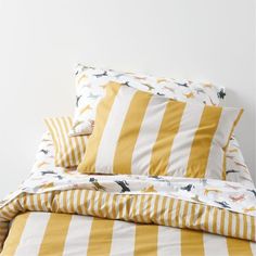 a bed with yellow and white striped sheets, pillow cases and pillows on top of it