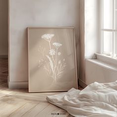 a white framed photograph sitting on top of a wooden floor next to a bed and window