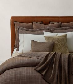 a bed with brown and white sheets and pillows on top of it, next to a wall