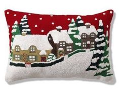 a red and white christmas pillow with houses on the snow covered ground in front of trees