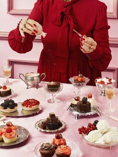 a woman in a red dress is eating cupcakes at a table with other desserts on it