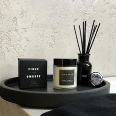 an assortment of candles, soaps and other items on a black tray next to a white wall