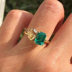 a woman's hand holding an emerald and diamond ring