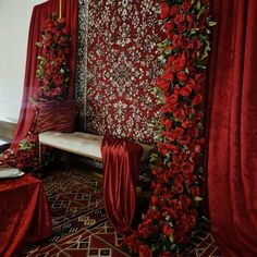 a room with red curtains and flowers on the wall, along with a white bench