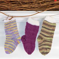 three knitted mittens hanging from a twig in front of a fireplace mantel