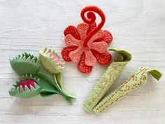 three different types of felt flowers sitting on a table next to each other, one red and one green