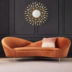 an orange couch in front of a black wall with a gold sunburst mirror