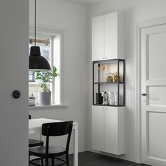 a room with a table, chair and shelves in it next to a door that has a potted plant on the window sill