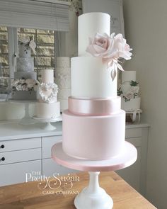 three tiered wedding cake with pink flowers on top and white frosting, sitting on a wooden table