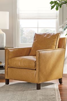 a brown leather chair sitting on top of a wooden floor next to a lamp and window